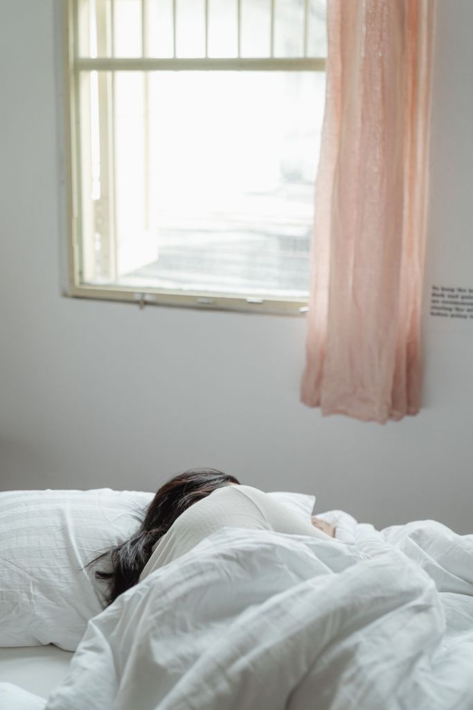 Frau schläft entspannt in einem sonnigen Schlafzimmer mit heller Bettwäsche