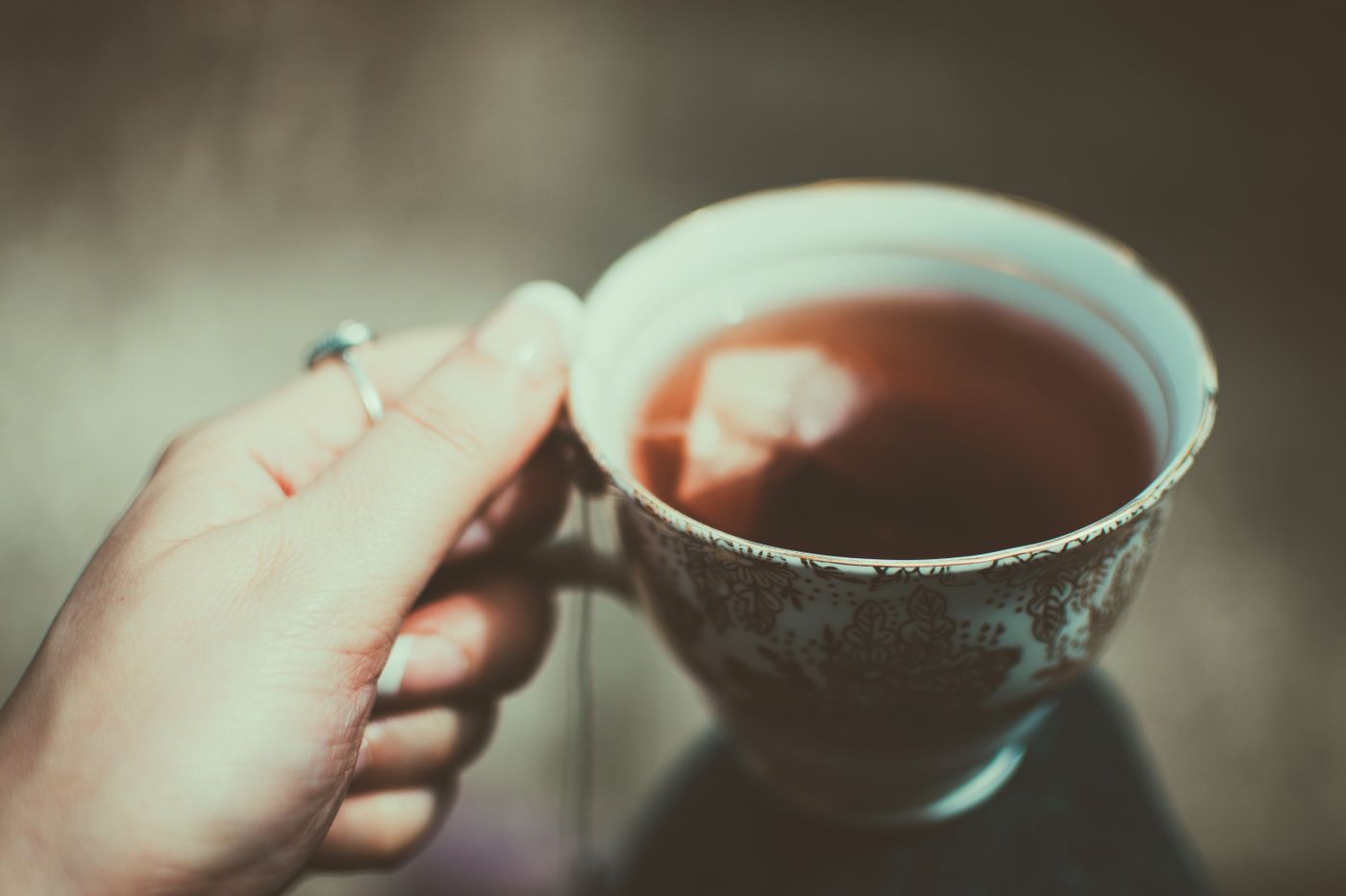 Hand hält eine verzierte Tasse mit heißem Tee in warmem Licht.